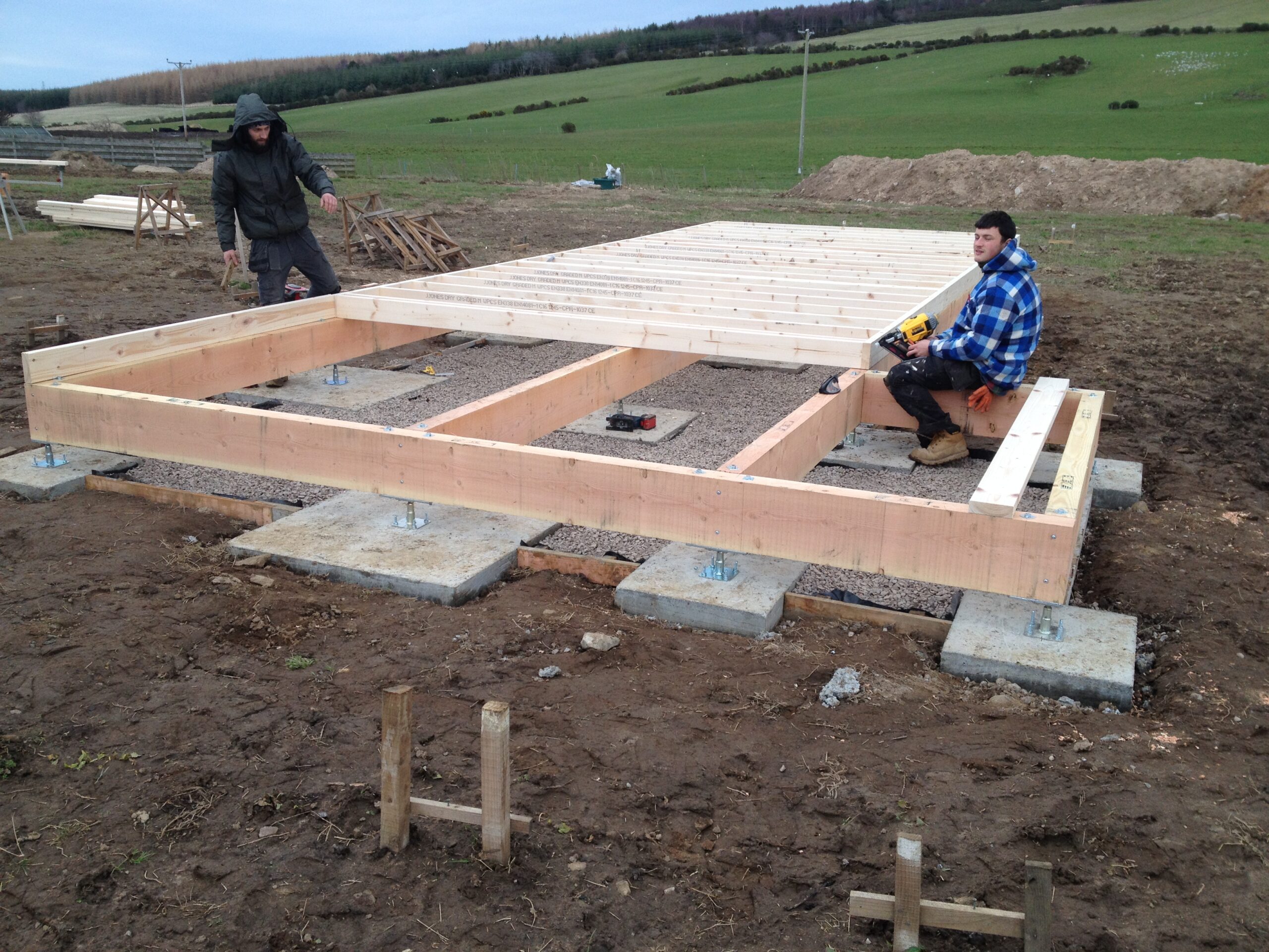 Adjustable metal anchors sit on concrete pads and support Douglas Fir floor beams, with joists going on.